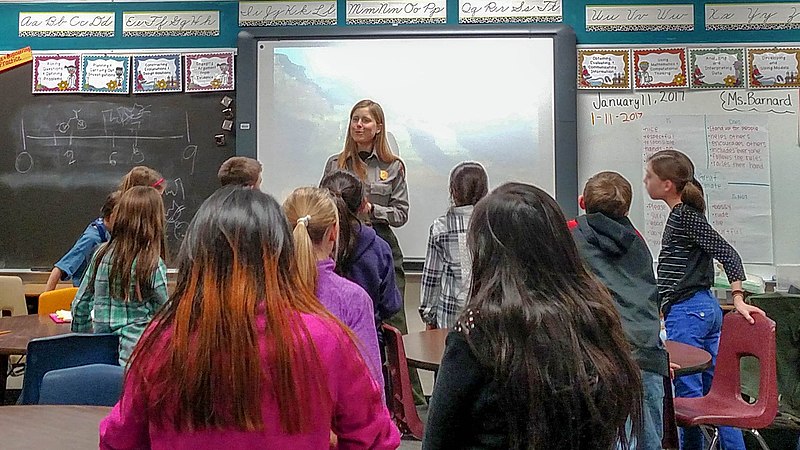 	 Students in a classroom, are interacting with a park ranger at the front of the room.